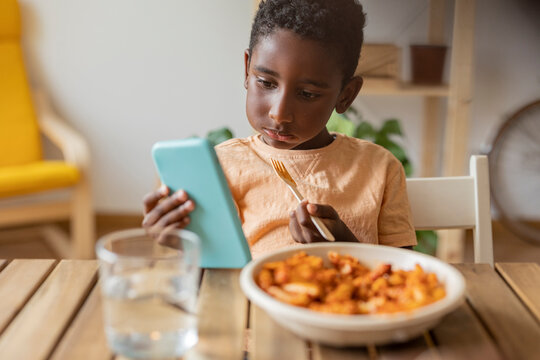 Boy eating food and using smart phone at dining table