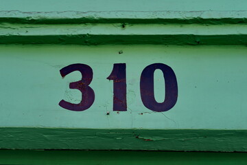 Numéro 310 peint en noir sur mur vert.