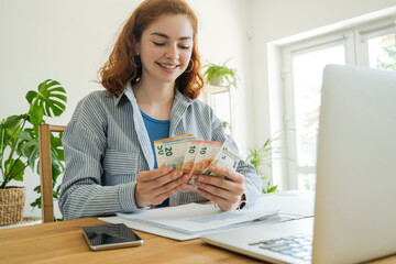 Happy young woman counting currency at home