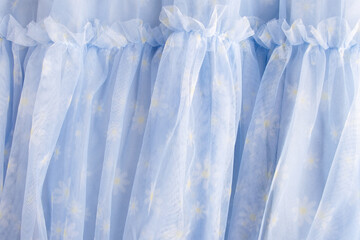 Flowered fabric. Sheer blue net-like tulle. The mesh fabric is folded in waves. White-blue veil or muslin.