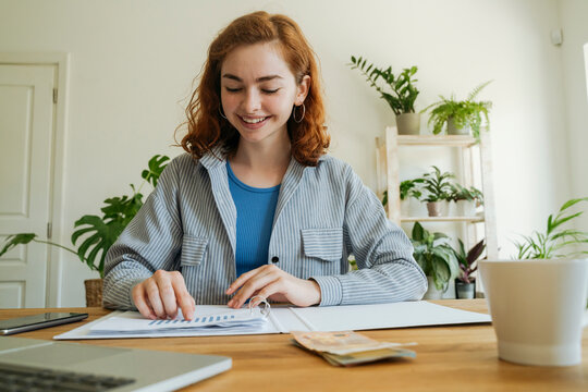 Happy young woman calculating financial graph at home