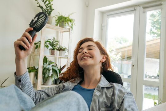 Happy woman with hand fan relaxing at home