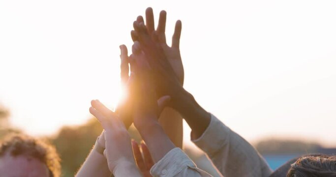 Multiracial group of diverse young people giving high five against a setting sun, feels excited close up focus on stacked palms during golden hour. Respect and trust, celebration and friendship