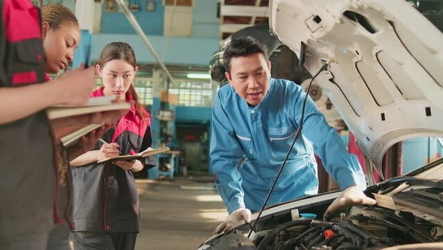 Asian male professional automotive engineer supervisor describes car engine maintenance and repair work with mechanic worker staffs team in fix service garage, specialist occupations in auto industry.