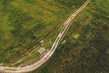 Aerial shot of curved dirt road through green grassy meadow, drone pov - Powered by Adobe