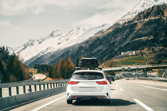 Rooftop cargo carrier bag. Rear view of a car with a roof box. Alpine highway. Black Roof Box on a Sporty White Wagon Family Car. Removable black car trunk for luggage on the roof of a car.