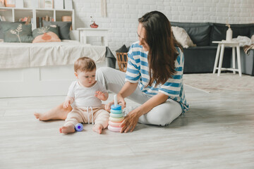 Beautiful young mother plays and teaches her baby 6 months old on the floor in the living room.mom and baby play with toys