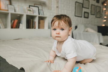 Portrait of a 6 month old crawling baby on the bed. the baby smiles and looks at the camera.