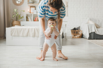 the concept of family, child, childhood, happy little child learns to walk with the help of mother at home