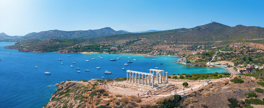 Panoramic view of the Temple of Poseidon at Cape Sounion at the edge of Attica, Greece, with moored sailboats in the bay during summer time
