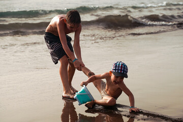 Boy pulling a brother during the game on the beach. Children have fun playing on the ocean. A fun...