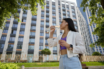 Beautiful young Vietnamese female drinking mineral water from a glass bottle on a walk. Portrait of...