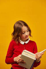 Portrait of happy schoolgirl reading a book on yellow studio