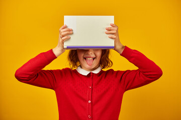 Portrait of happy teenage schoolgirl cover her face by book