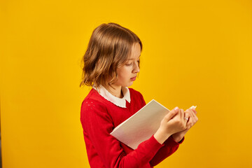 Portrait of happy schoolgirl reading a book on yellow studio