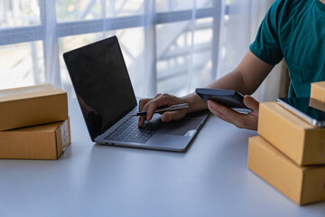 Asian male entrepreneur working sme business selling online at home with parcel boxes for delivery