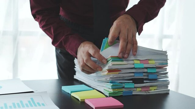 Businessman working in stacks of paperwork files for searching information unfinished documents about pile audit form on desk office and investigate financial doc in busy workload.