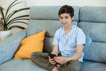 Close-up portrait of a teenage boy, with a phone in his hands, sitting in his room and looking at a camera