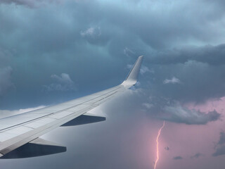 Fototapeta na wymiar Aircraft wing slicing through thunderstorm sky, as airliner takes flight.
