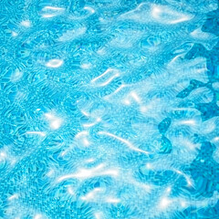 Water in swimming pool. Water surface background with sun reflections and ripples.