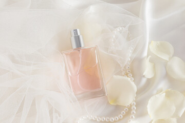 A chic bottle of women's perfume or eau de parfum with a delicate smell of roses lies on a satin fabric of the color of cream and rose petals.