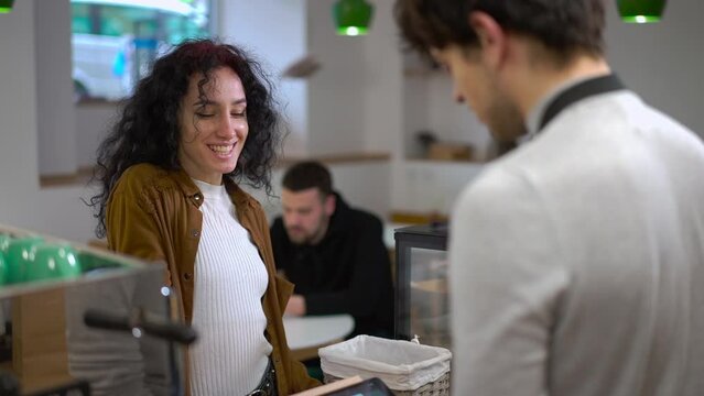Positive young woman smiling talking with man ordering coffee in cafe. Charming Caucasian female client and male barista in the morning in urban city
