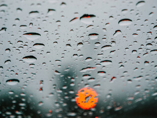 Raindrops drench the car window as red light bokehs shine. The monsoon seasons motoring beauty...