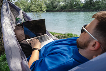 Relaxing work environment: man in hammock with laptop by river