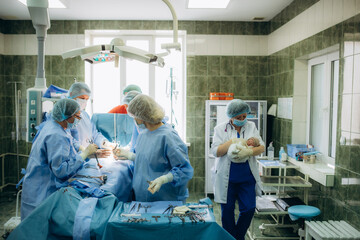 surgeons perfoming surgery operation of abdominal cesarean section during child delivery birth at clinic operating room. - obrazy, fototapety, plakaty