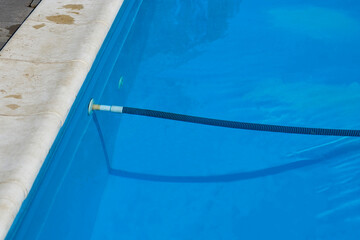 Summer pool edge with blue water and filling or cleaning hose