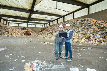 two workmen looking at laptop in recycling center - obrazy, fototapety, plakaty