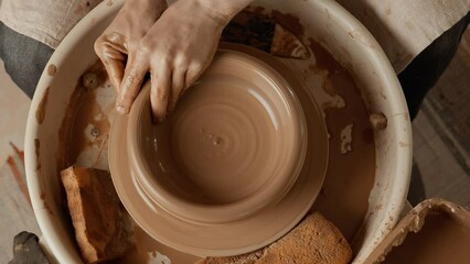 Potter making ceramic bowl or plate on pottery wheel. Top view. Potter shapes clay product. Two hands create bowl. Close-up in 4K, UHD
