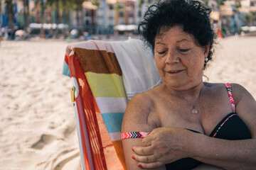 Older woman protecting her scar from shoulder surgery. Woman on the beach taking care of her scar...