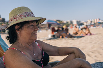 Woman with hat relaxed sitting on beach chair. Older lady on vacation watching the sea while...