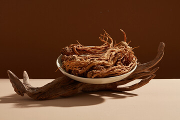 Front view of angelica sinensis roots on round white plate and dry twig decorated on dark...