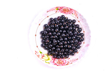 black currant berries in a plate isolated on white top view