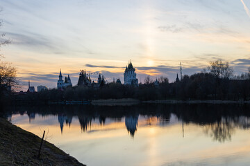 Fototapeta na wymiar Calm piver, silhouettes of trees and towers of the Izmailovsky Kremlin in Moscow at sunset. Reflection in water.