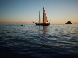 Fototapeta na wymiar Sailing vessel gliding across a vast expanse of blue water, with a cloudless sunset sky