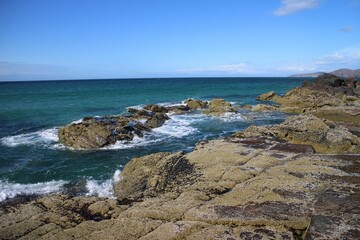 Landscape of a rocky shore surrounded by the sea under a blue sky and sunlight
