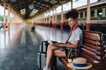 Asian teenage girl african american traveling using computer laptop while waiting for a train at a station.