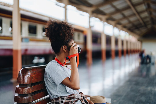 Asian teenage girl african american traveling using a camera take a photo to capture memories while waiting for a train at the station.