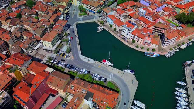 Aerial view of the sea water canal in the city center where fishing boats and amateur sailing yachts are moored. Small classic fishing boats with nets. Little Venice. Grado Italy 07.2023