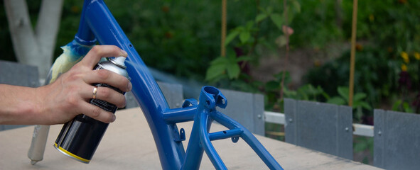 the father paints the child's bicycle with blue paint.
