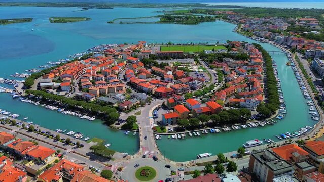 Aerial view of the old city. Roofs of buildings with red tiles and many chimneys. The bell tower of the Catholic Cathedral in the city center. Traveling through narrow streets. Italy Grado 09.2023
