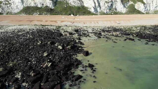 Drone footage over sea water moving to rocks under white cliffs of Samphire Hoe in Dover, England