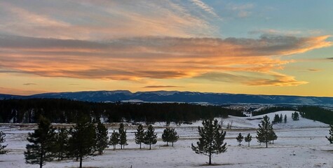 Tranquil landscape featuring a vibrant sunset in the sky above a rolling meadow surrounded by hills