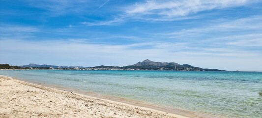 Sandy beach and crystal clear, blue waters lapping against the shore. Alcudia, Balearic Islands.