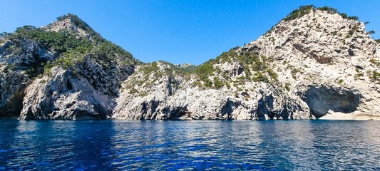 Two green cliffs with blue waters in the foreground. Alcudia, Balearic Islands.