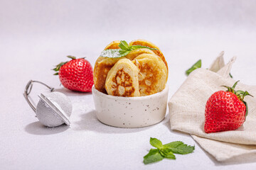 Cottage cheese pancakes, syrniki, curd fritters with strawberry, mint and powdered sugar in a bowl