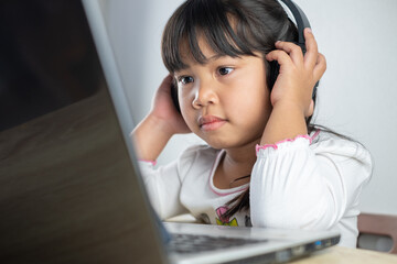 4-5 years old Asian girl wearing white shirt is studying online via computer using bluetooth...
